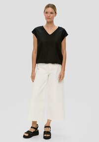 Zwarte linnen V-hals top met kapmouwen, gecombineerd met witte wijde broek en zwarte platform sandalen. Eenvoudig ontwerp, lichtgewicht stof.