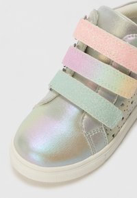 Sneaker met een metallic, iriserend bovenwerk voorzien van drie sprankelende Velcro-straps in pastelkleuren. Witte rubberen zool met textuurdetails.