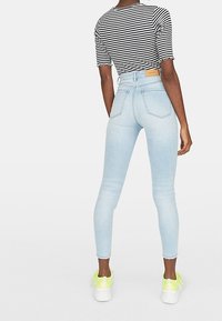 Jeans ajustados de denim azul claro con cintura alta, que presentan una textura desgastada y bolsillos traseros tradicionales. Combinados con una camiseta a rayas y zapatillas.