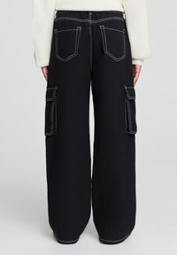 Czarne szerokie spodnie cargo z kontrastowymi białymi szwami. Posiadają dwie boczne kieszenie cargo i dwie tylne kieszenie. Elastyczny pas.