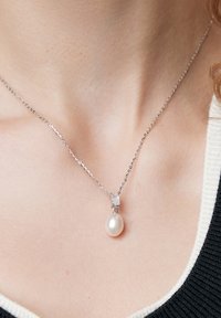 Srebrny naszyjnik z łańcuszka z dużym białym perłą jako zawieszką oraz małym prostokątnym kryształowym akcentem ponad perłą.