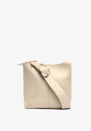 Beige læder skuldertaske med en glat tekstur, der har en bred rem og en cirkulær sølvspænde detalje. Designet er enkelt og struktureret.