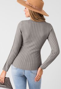 Maglione lungo a maniche ribbed grigio con un design aderente e scollatura a barca. La texture presenta linee verticali in rilievo, abbinato a jeans azzurri.