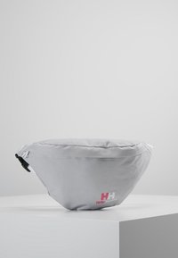 Sac banane en tissu gris avec une forme arrondie, comportant un logo rose et blanc, une sangle ajustable et une texture lisse.