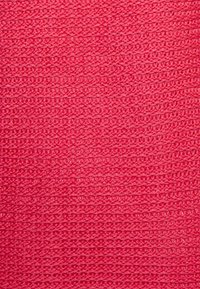 Tela texturizada en un vibrante color rosa, con un patrón de punto con filas uniformemente espaciadas y apariencia suave. El material sugiere suavidad y flexibilidad.