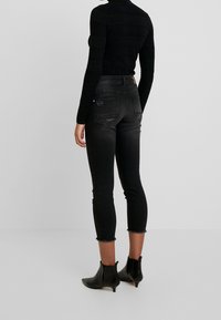 Jeans skinny negros con detalles desgastados y bajos deshilachados, hechos de una mezcla de algodón. Combinados con botas negras hasta el tobillo.