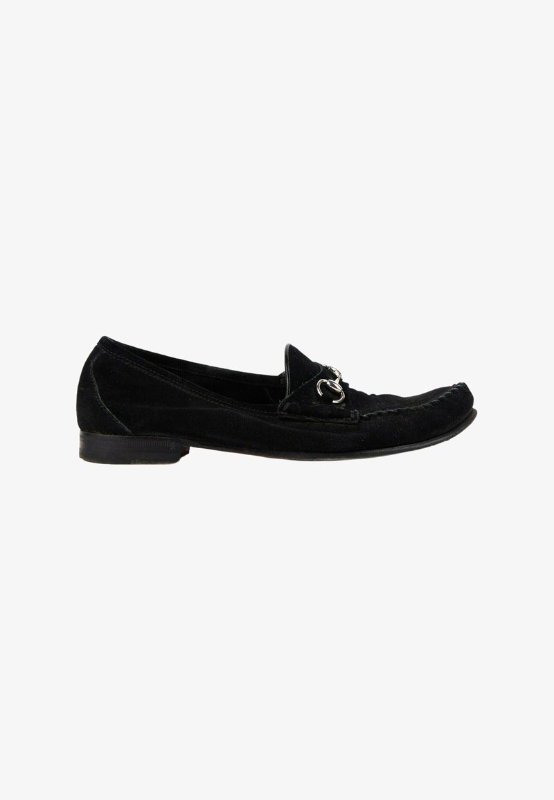 Mocassin en daim noir avec un petit talon et un détail mors argenté sur le dessus, montré de côté sur fond blanc.