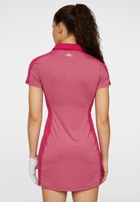 Rosa golfklänning gjord av stretchigt tyg med polo-krage, korta ärmar och sidopaneler i en mörkare nyans av rosa. Har en logotyp på ryggen.