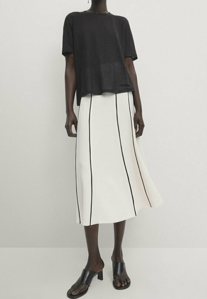 Schwarzes kurzärmeliges Oberteil kombiniert mit einem weißen Midirock mit vertikalen schwarzen Streifen, ergänzt durch schwarze offene Mules.