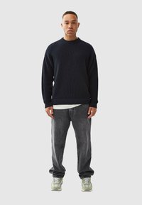 Dark navy knitted sweater with a crew neck, paired with loose grey jeans and green-tinted sneakers. Textured fabric, relaxed fit.