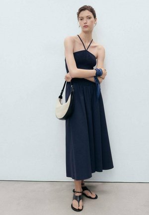 Donkerblauwe strapless top met een gestructureerd ontwerp, gecombineerd met een vloeiende, enkel-lange donkerblauwe rok. Geaccessoireerd met een zwart-witte handtas en zwarte sandalen.