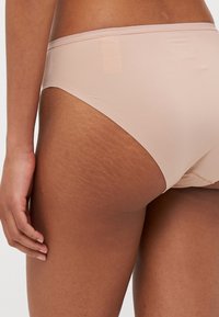 Nude bikini Calvin Klein s hladkým, elastickým materiálom a nízkym pásom. Má minimálne švy a pás s potlačou loga.