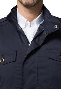 Granatowa kurtka z wysokim kołnierzem, zamkiem błyskawicznym i dwoma przednimi kieszeniami. Posiada metalowe akcenty w postaci guzików oraz gładką, trwałą teksturę materiału.