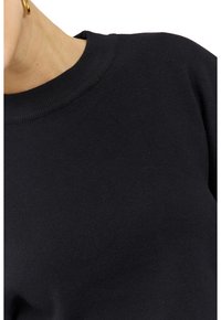 Pull noir en maille avec un col rond côtelé et un tissu texturé. Le design est minimaliste, sans motifs apparents ni éléments métalliques.