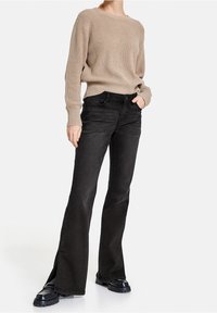 Suéter de canalé beige, jeans negros acampanados con aberturas laterales y zapatos negros gruesos. Los jeans cuentan con bolsillos frontales y una cintura ajustada.
