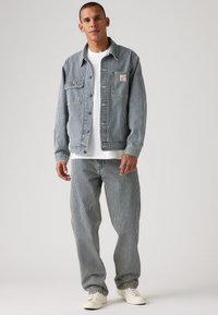 Chaqueta y pantalones de mezclilla a rayas en azul y blanco. La chaqueta tiene dos bolsillos en el pecho, cierre de botones y un parche de logo. Se complementa con una camiseta blanca.