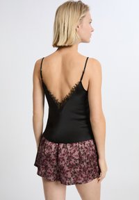 Camisole nera in satin con scollo a V profondo e bordo in pizzo, abbinata a una gonna rosa trasparente con motivo floreale e design svasato.