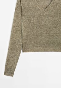 Pull court à manches longues avec col en V, tricoté dans un tissu chiné marron clair, posé à plat sur un fond blanc.