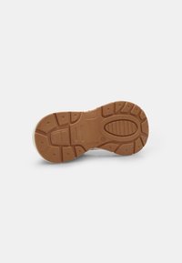 Kummi sneakerite alus, millel on tekstureeritud pruun muster, mis sisaldab sooni ja tõstetud elemente haardeks ja libisemiseks. Siledad servad, ilma nähtavate logodeta.