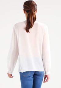 Vit chiffongblus med långa, puffiga ärmar. Har en rak fåll och elastiska manschetter. Matchas med en blå denim underdel.