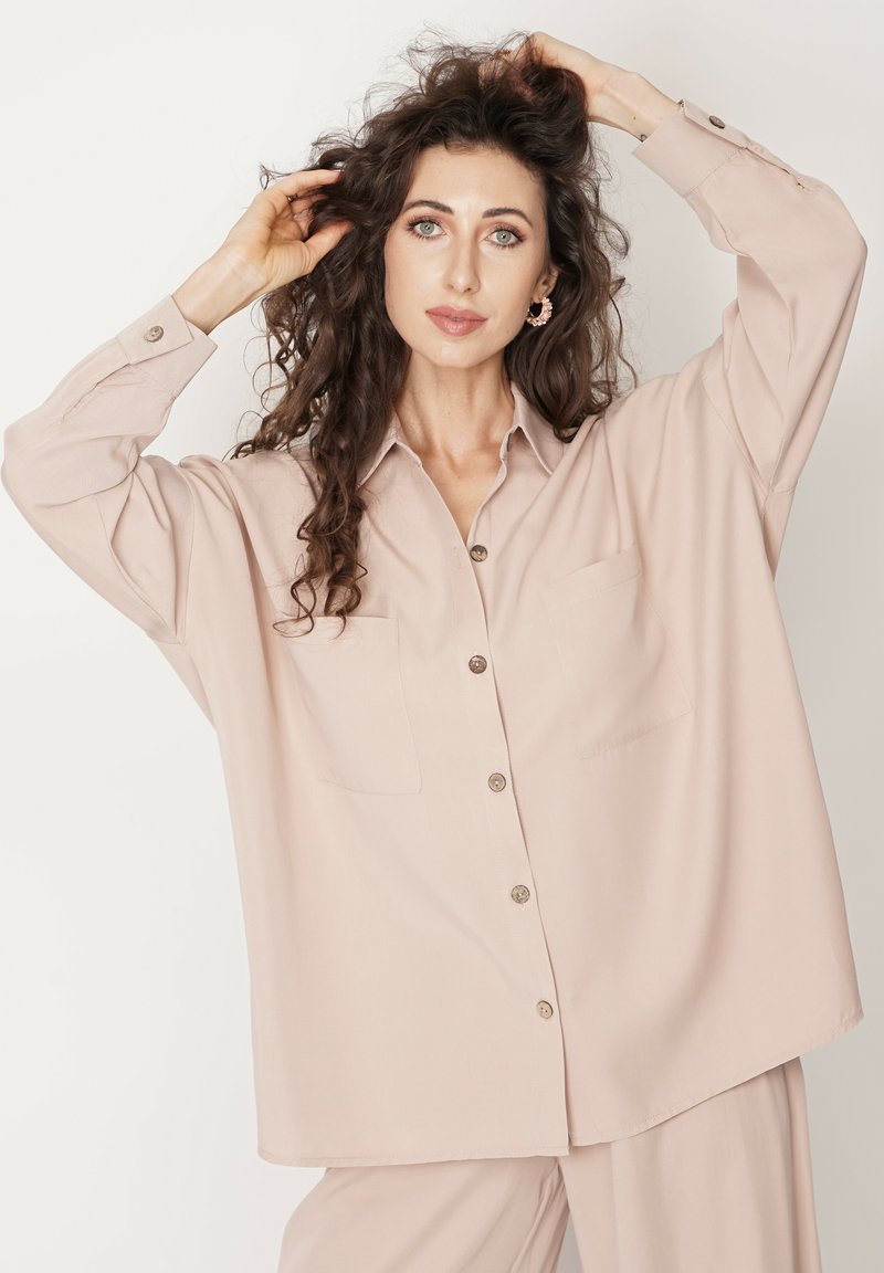 Jasno beżowa, oversize koszula zapinana na guziki, z dwoma kieszeniami na piersi, miękką teksturą tkaniny, długimi rękawami i klasycznym kołnierzem.