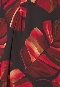 Tyg med djärv röd och brun tropisk bladmönster på en mörk bakgrund, som visar veck och struktur.