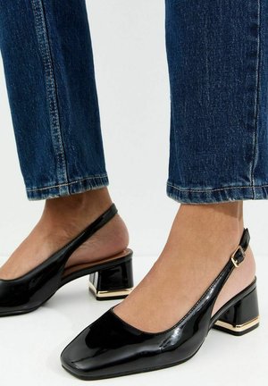 Décolleté slingback in vernice nera con fibbia dorata e tacco a blocco indossate con jeans blu.