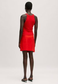 Red knitted tank top with wide straps, paired with a red mini skirt. Smooth texture, fitted design, and minimal embellishments.