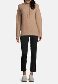 Beige ribbad tröja med hög krage och dragsko, kombinerad med svarta slim-fit byxor och ljusa träningsskor.