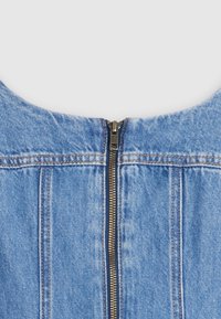 Denims ražojums ar apaļu izgriezumu, centrā ar rāvējslēdzēju un vertikālām šuvēm. Gaiši zila krāsa, mīksta tekstūra un zelta akcenti.