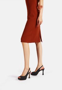 Décolleté neri slingback con punta chiusa, tessuto texture e tacco affusolato. Modella che indossa un abito brown aderente.