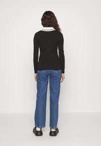 Haut noir à manches longues avec un col blanc, associé à un jean en denim bleu ample et des chaussures noires, vu de l'arrière.