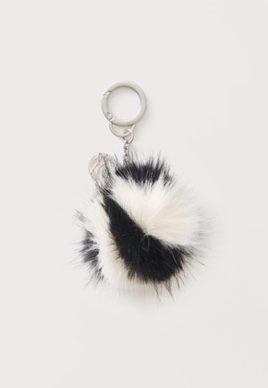 Sort-hvidt fluffet pom-pom nøglering med en sølv metalring og kæde på en ensfarvet lys baggrund.