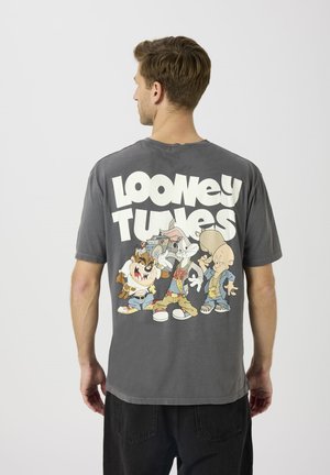 Harmaa puuvillainen t-paita, jossa on sarjakuvamainen Looney Tunes -hahmojen kuva ja selässä paksu valkoinen teksti. Lyhyet hihat ja rento istuvuus.