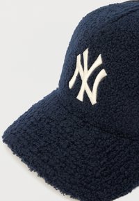 Granatowa czapka z daszkiem z polaru o teksturowanej powierzchni, z haftowanym białym logo na przodzie i zakrzywionym daszkiem.