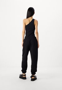 Svart top med ena axeln och svarta smala sweatpants. Slätt tyg med elastisk midja. Kraftiga svarta skor med ankelsnören.