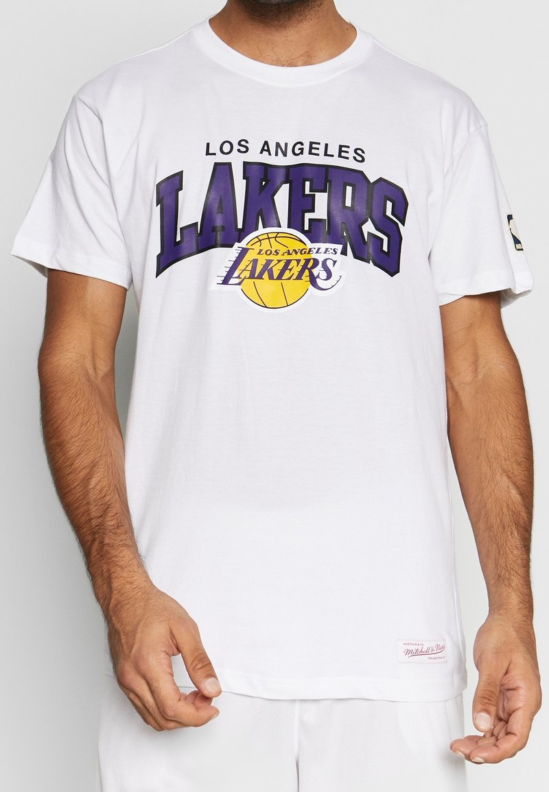 Hombre vestido con una camiseta blanca que tiene un gran texto púrpura "Los Angeles Lakers" y un logo de baloncesto amarillo en el frente.
