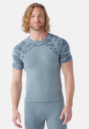 Lichtblauw thermoshirt met korte mouwen en een gestructureerd camouflagedesign aan de bovenkant. Zacht, aansluitend ontwerp met ribstof bij de mouwen en de zoom.