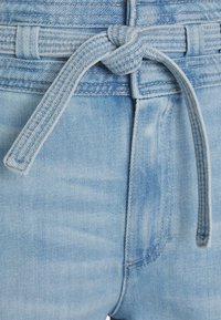 Pantalones cortos de mezclilla azul claro con una cinturilla anudada y tejido texturizado. La vista en primer plano resalta el color y los detalles del material.