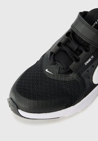 Schwarzer Sportschuh mit einem oberen Teil aus Mesh, strukturierten Akzenten und einem weißen Logo. Er hat Schnürsenkel und ein dynamisches Fit-Gurt-Design.
