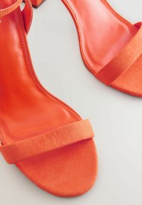 Orange öppna sandaler med tå öppet som har en slät läderövre och ett mjukt, texturerat rem. Fyrkantiga klackar och en minimalistisk design.