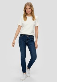 Chemise blanche à manches courtes associée à un jean skinny bleu foncé et des baskets blanches. La tenue présente un design simple et ajusté.