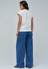 Hvid bomulds t-shirt med korte, rullede ærmer, parret med højtaljede, vide blå denimjeans med opsmøg.