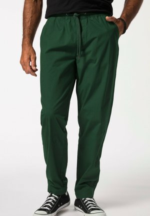 Green, tapered pants with an elastic drawstring waist, side pockets, and a smooth texture. Worn with black sneakers.