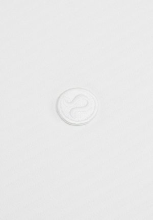 Biely textil s jemnou diagonálnou štruktúrou obsahuje v strede vyšívané kruhové logo, ktoré zobrazuje hladký a vystúpený dizajn.