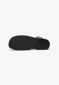 Suela de zapato negra con una superficie lisa y plana. Presenta una ligera curva en la puntera y un patrón de agarre texturizado para mayor tracción.