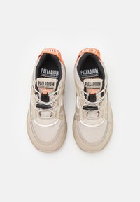 Adidași impermeabili bej, cu un superior texturat, șireturi negre și accente portocalii strălucitoare pe călcâi și limbă. Logo-ul este afișat proeminent.