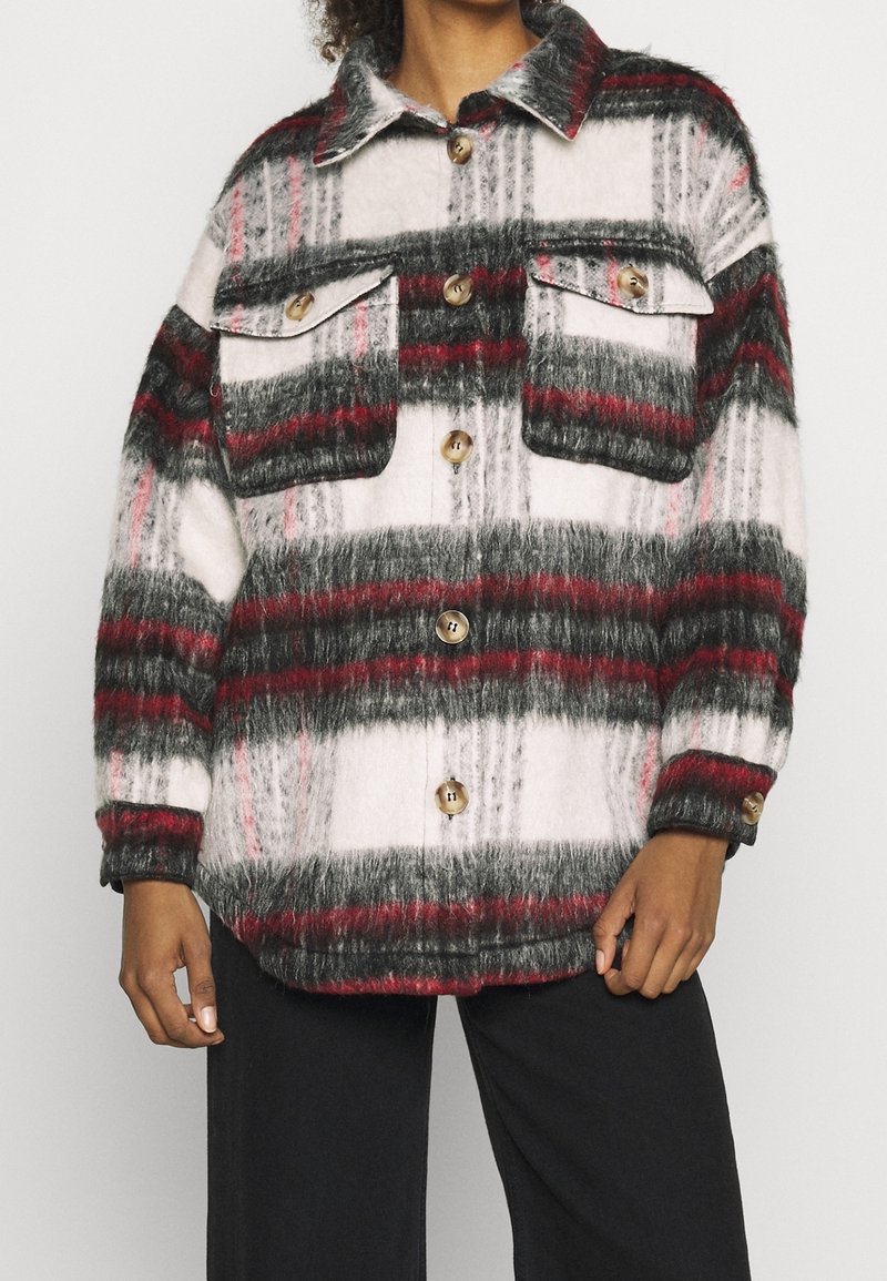 Rutigt skjortjacka med lång ärm i vitt, svart och rött, med en mjuk, luddfäst yta, två bröstfickor och stora beige knappar.