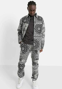 Zwart-wit gestreepte shirt- en broekset, met bloem- en paisleypatronen, gemaakt van lichte stof, gecombineerd met witte sneakers.