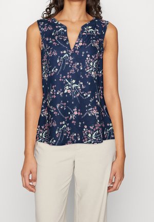 Haut bleu marine sans manches avec imprimé floral rose et blanc, porté avec un pantalon beige clair, visible du cou jusqu'aux hanches.